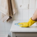 A person wearing hand gloves cleaning a white surface